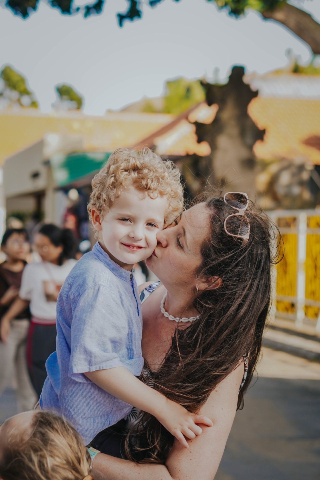 Mother kissing her son during a candid family session on a Bali street near a temple