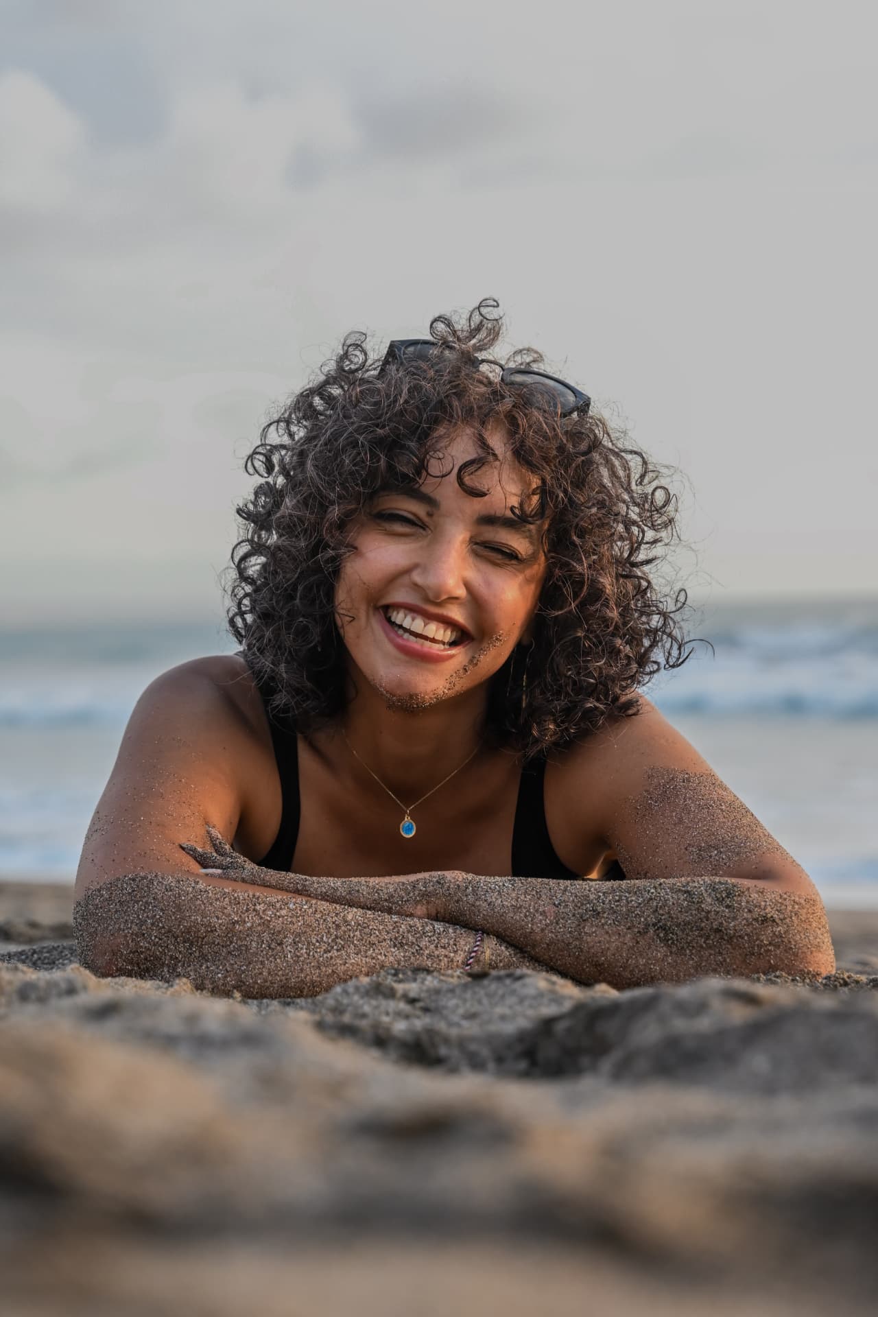 Bali personal photography — joyful curly-haired woman portrait lying on a sandy beach at sunset