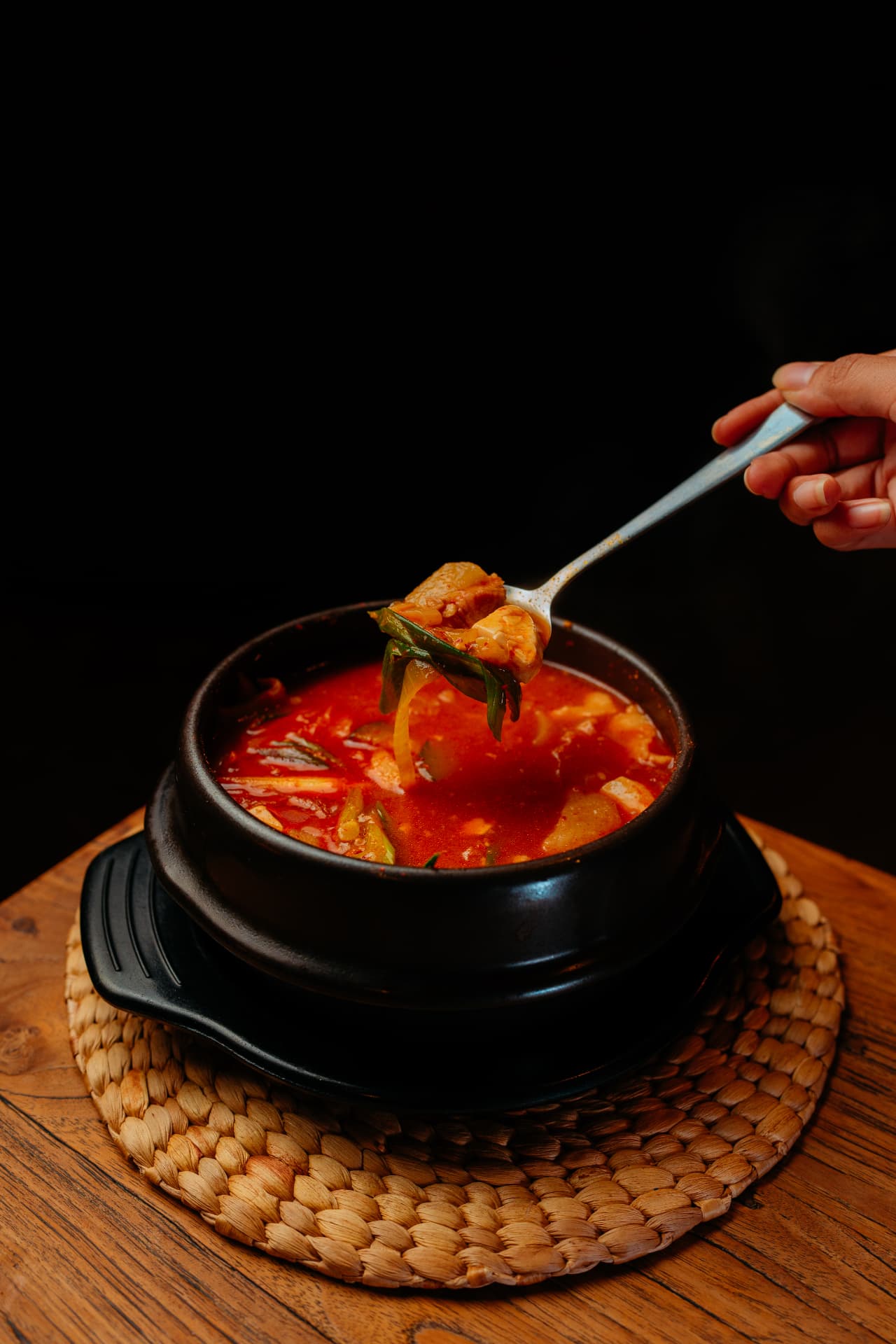 Steaming Korean kimchi stew served in a clay pot, dark food photography in Bali